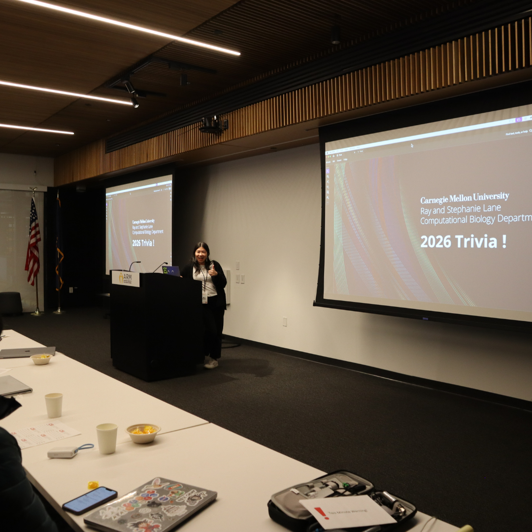 A woman pointing at the camera in front of a projector smiling at the camera