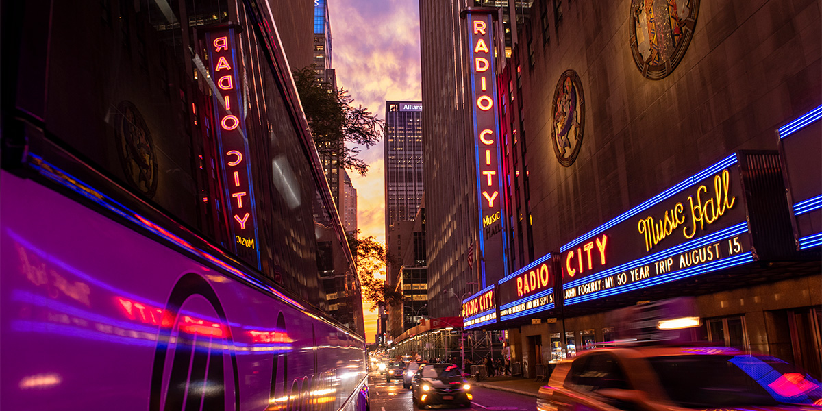 Photo of the neon lights from Radio City Music Hall reflecting off of a passing bus.