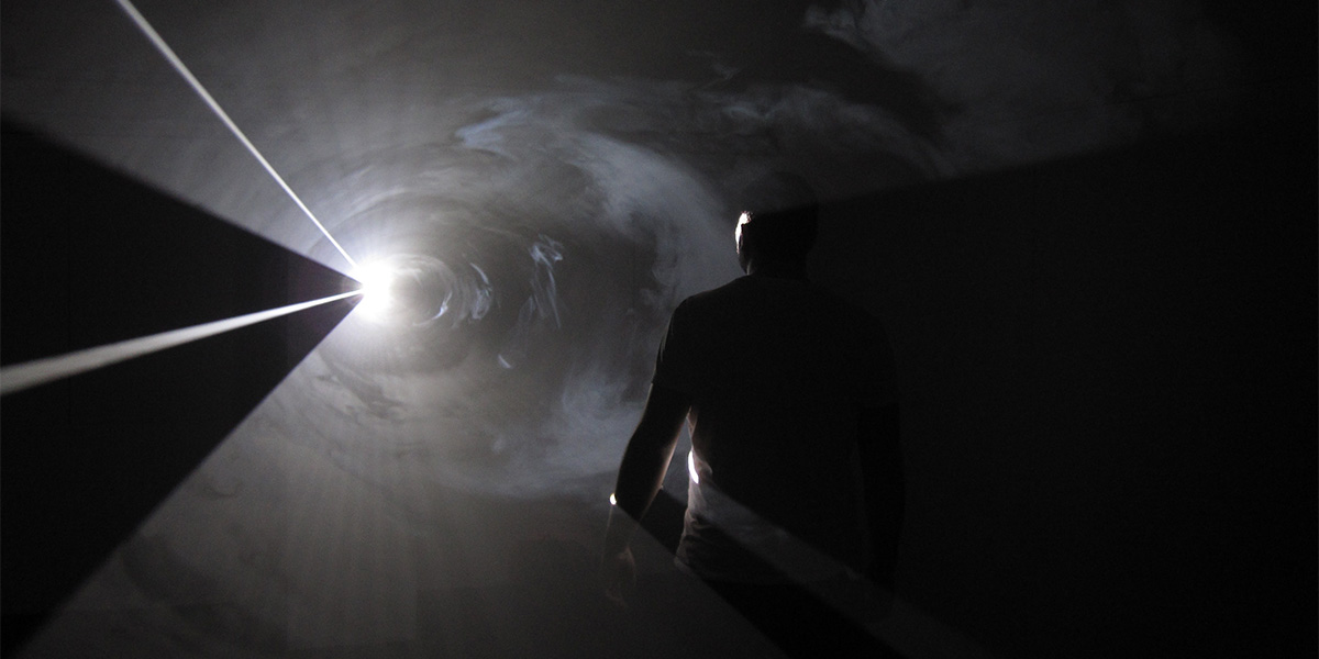 Photo of a man walking into a bright light with a very dark background.