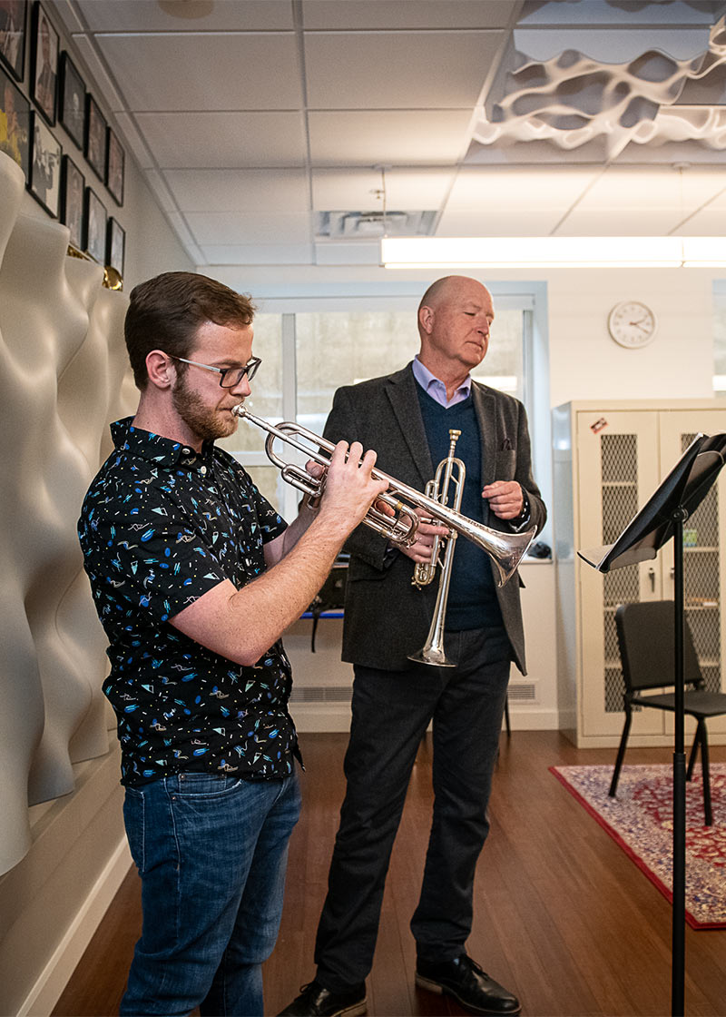 Photo of a student playing a trumpet in a private lesson with a professor.