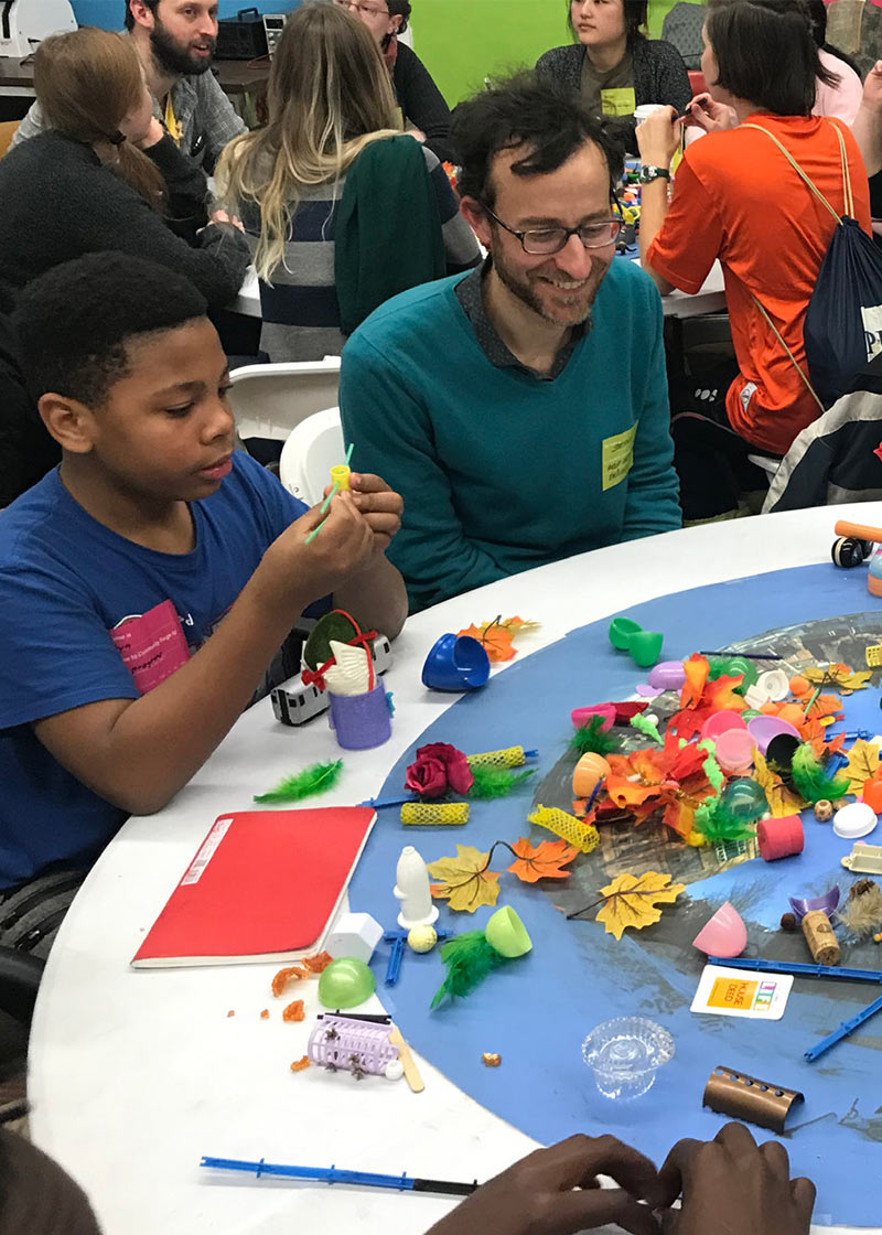 A child from the community sitting around a table with an architecture student, working through a creative exercise.