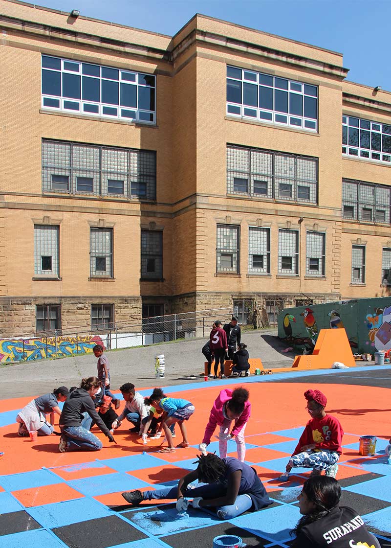 Child and adult community members, painting the concrete at the Community Forge.