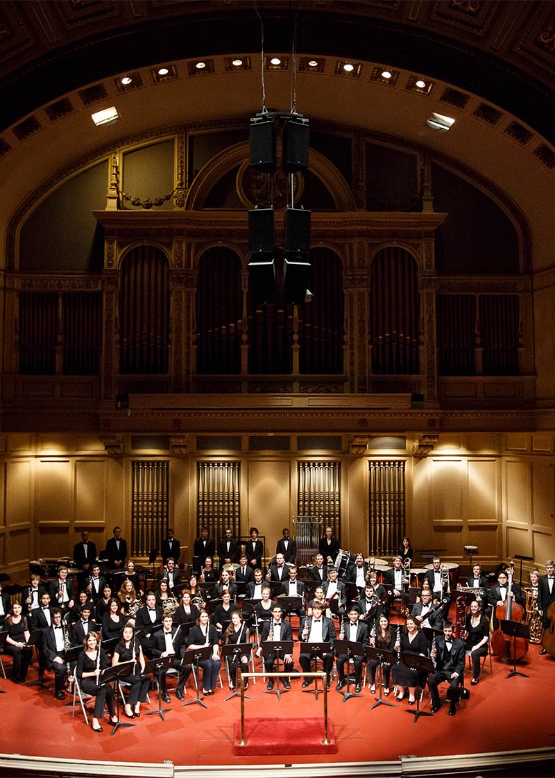 The Wind Ensemble, on stage with their instruments, posing for a photo.