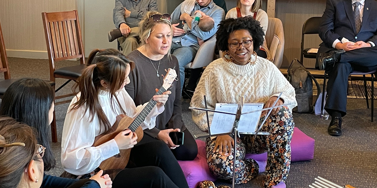 Group of women playing music, as community members gather and listen.