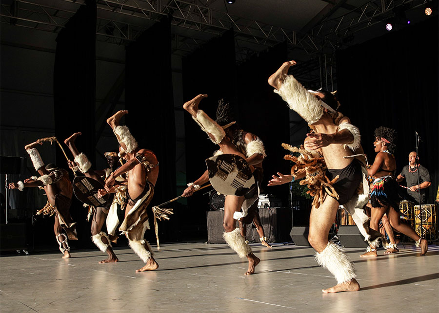 A line of 5 men in a line, kicking high.