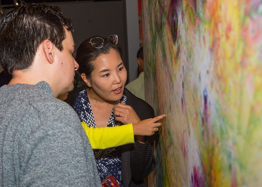 A child points to a painted canvas, while two adults appear to be considering what the child is communicating.