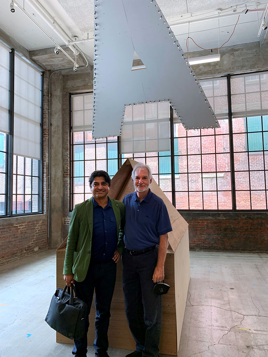 Paul and Omar with a large A and a structure made from plywood in the background.