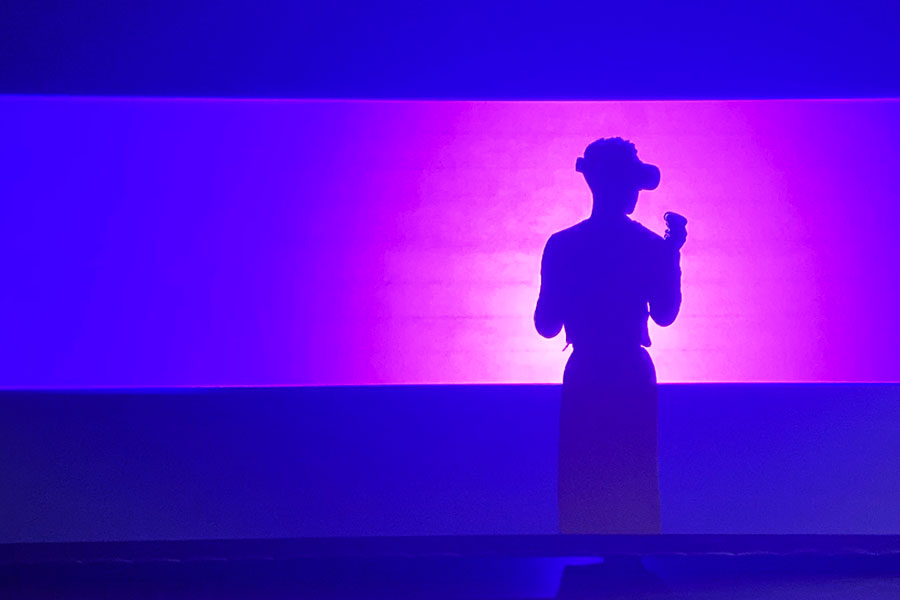 A person wearing a virtual reality headset and controller against a lighted, purple background