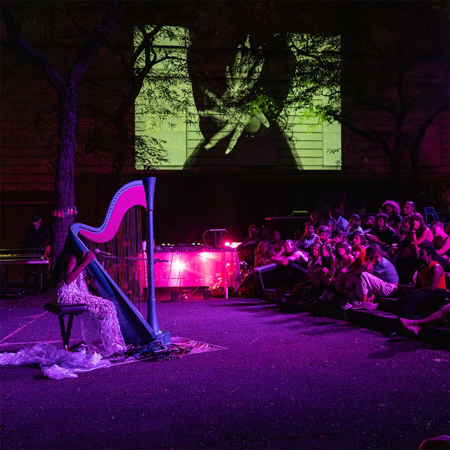 Performer playing a harp in the courtyard, as art is projected on the side of the museum.