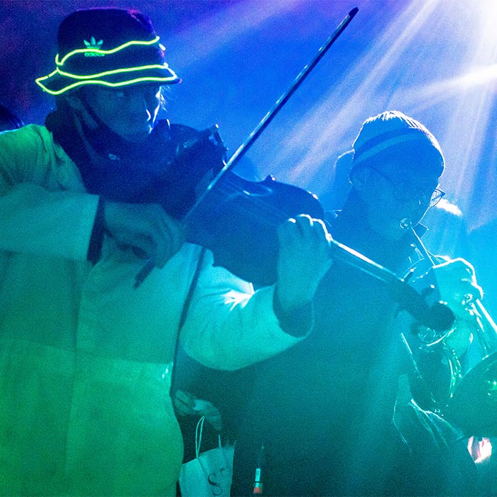 Two students playing instruments, bathed in blue and green lights.