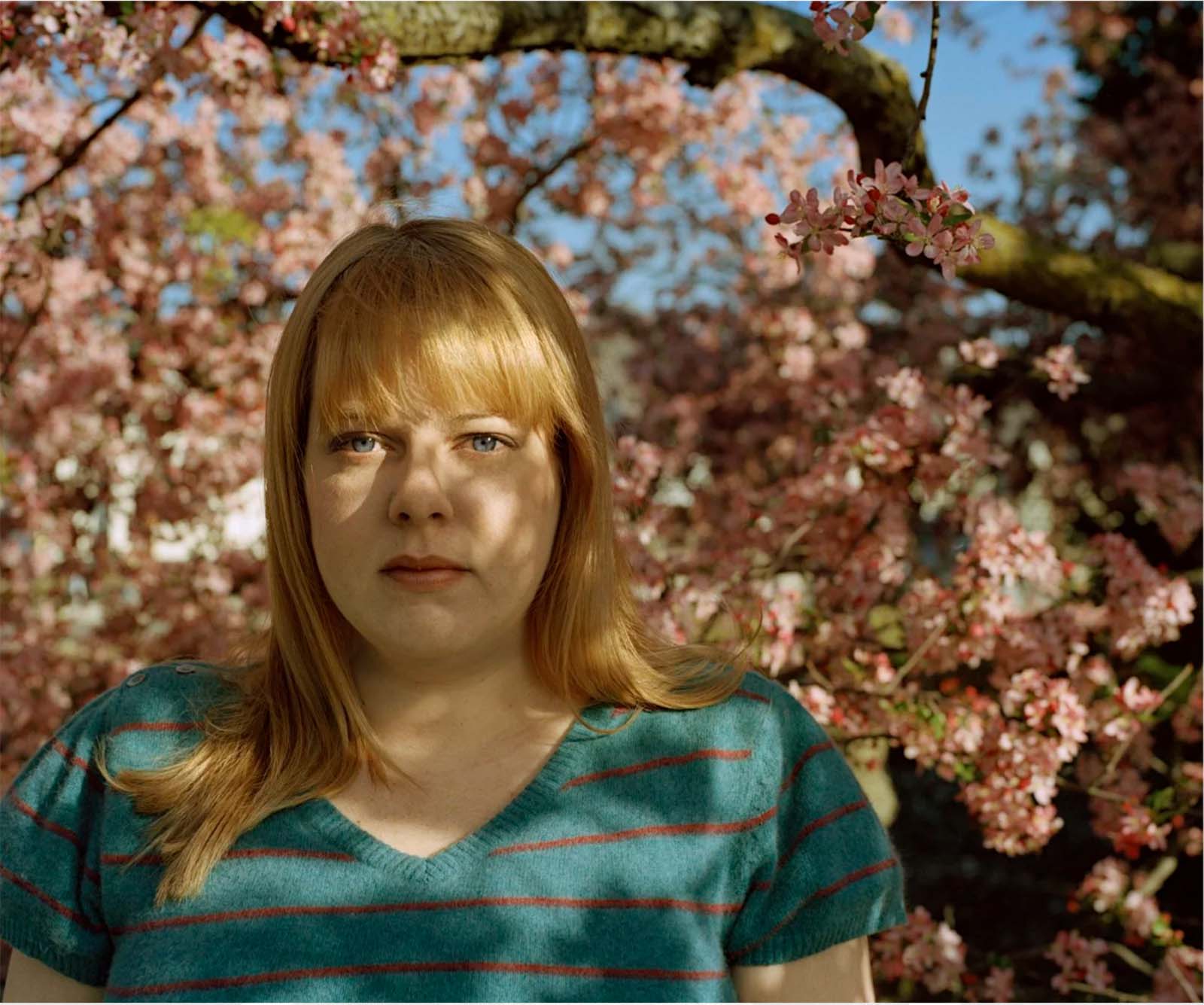 Photo of a woman standing amidst cherry blossoms in bloom.