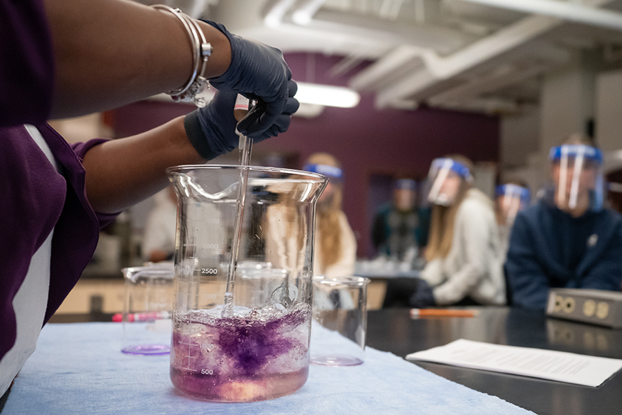 Image of hands pouring a purple liquid into a round, squat beaker