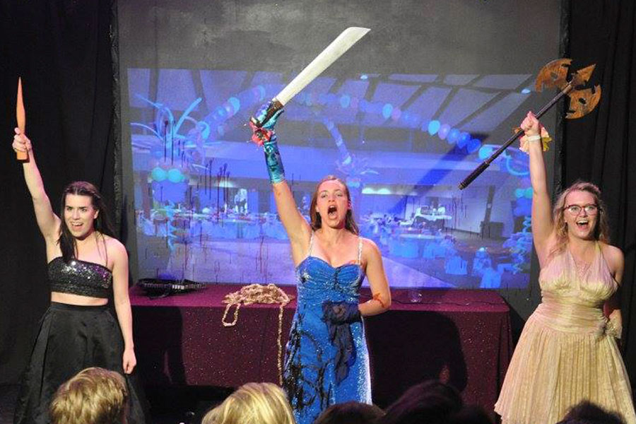 Three Women in evening gowns on a stage wielding a dagger, a sword, and an ax