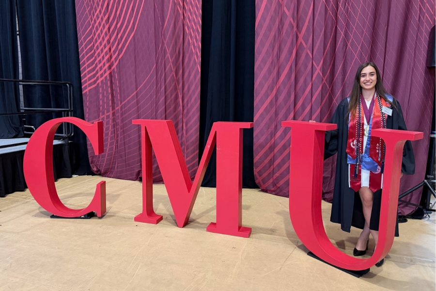 Aleksaundra Handrinos in commencement regalia posing with large CMU letters