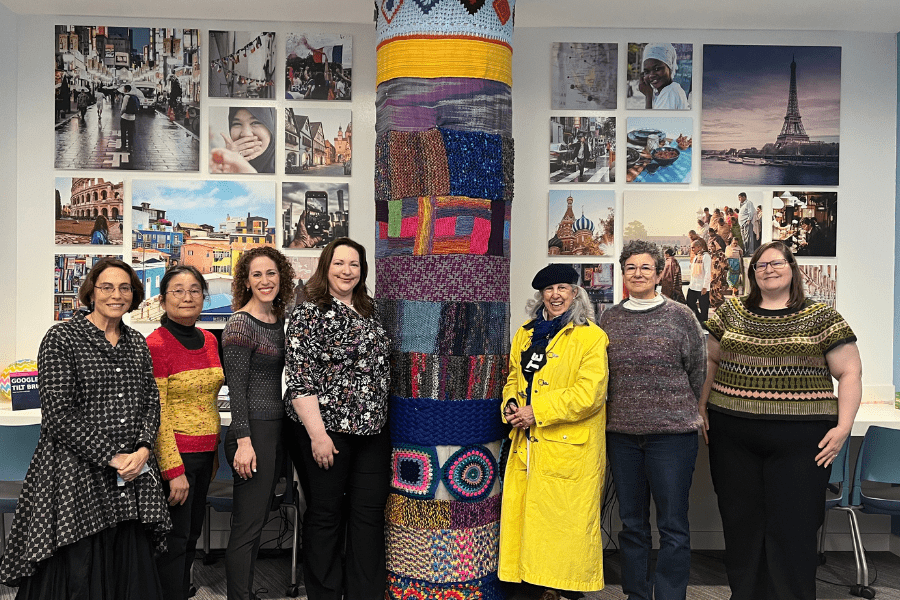 CMWA knitters stand with their artwork on the big concrete pillar in the Askwith Kenner Global Languages and Cultures Room
