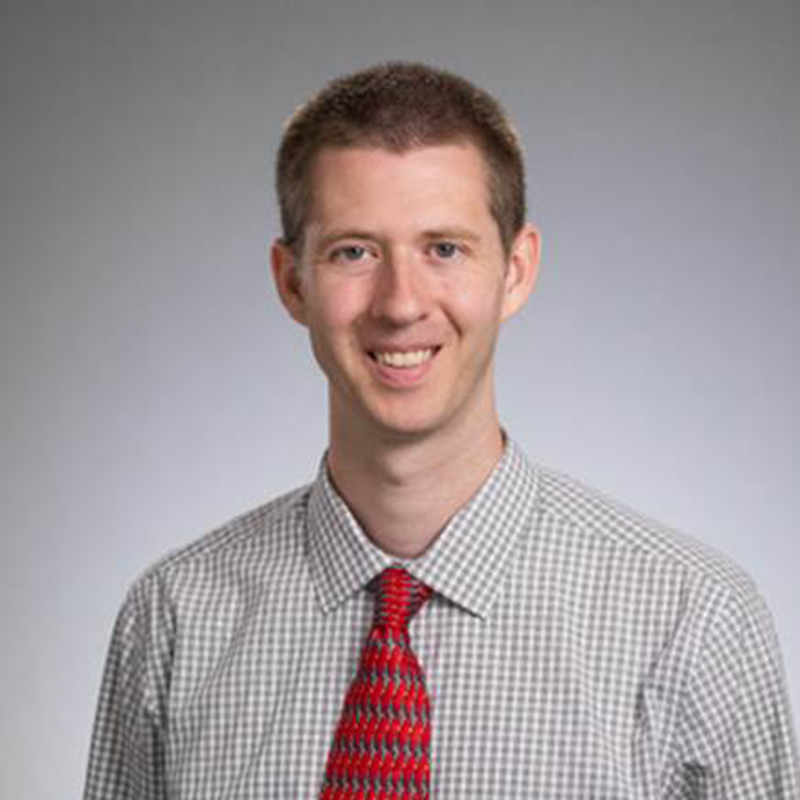 Headshot of a man wearing a red tie and a checkered dress shirt smiling for the camera