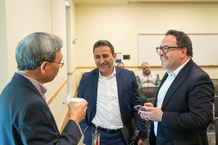 Three men in business suits smile and talk together during the AI and DA Summit.