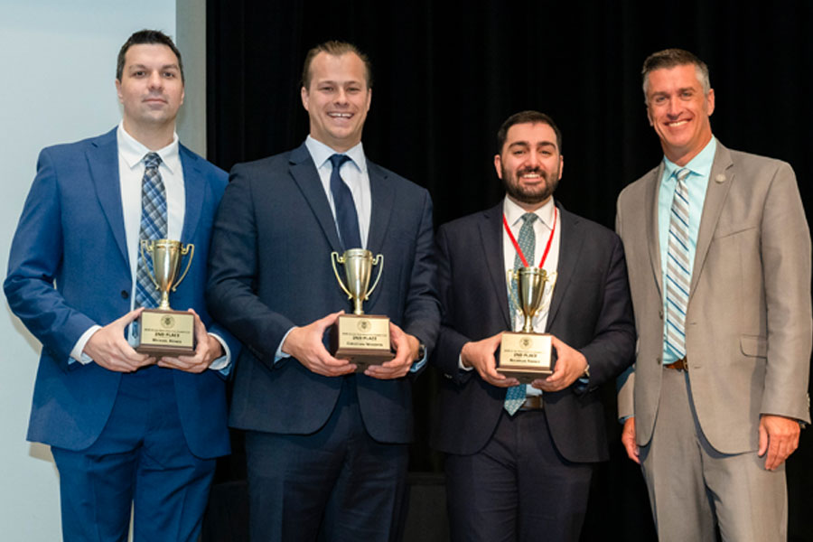 Three award winners stand on stage holding their second-place trophies.
