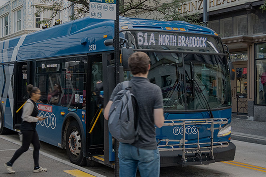 Pittsburgh Regional Transit bus arriving at a downtown bus stop with passengers waiting to board.