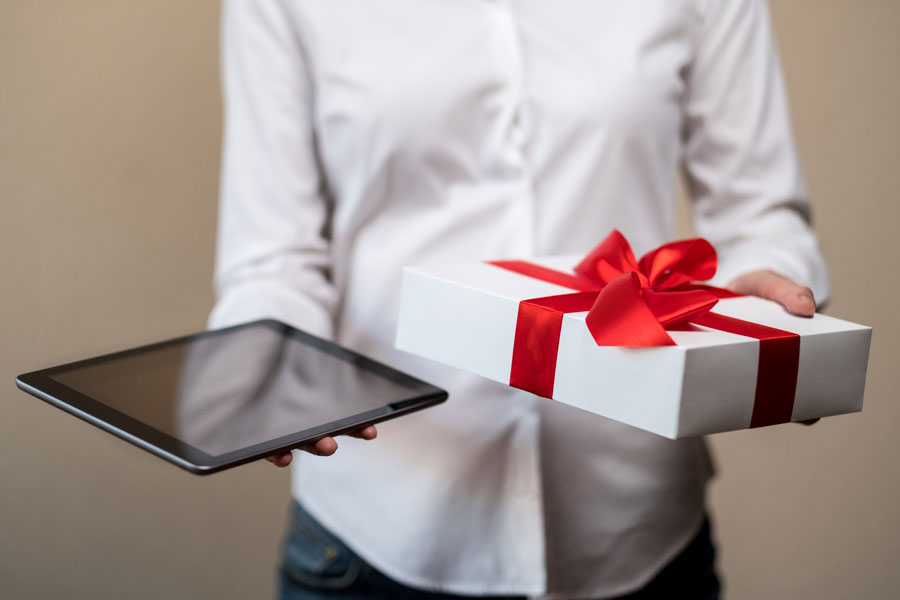 Individual in white shirt holding an iPad in one hand and a present in the other.