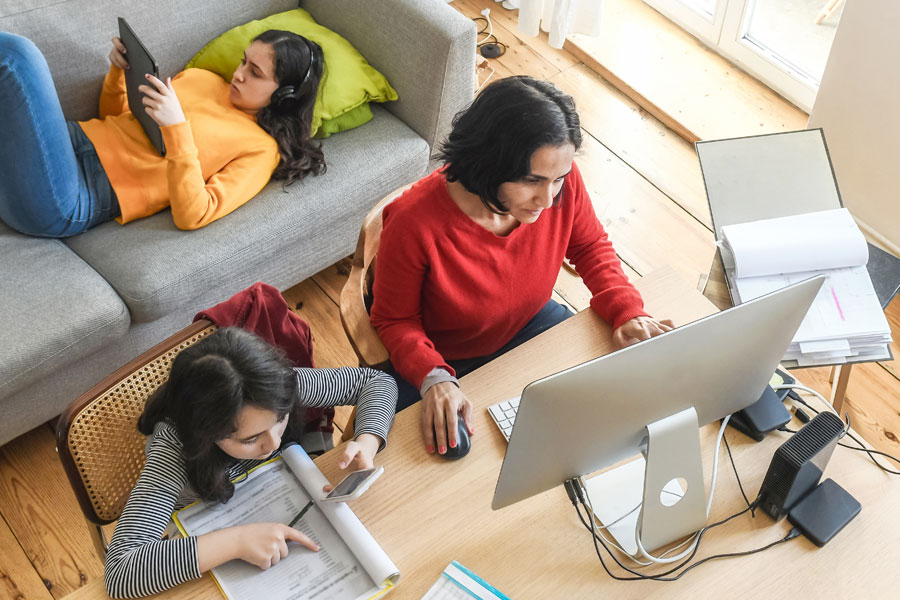 Woman workig fro home with two children working remotely in the room.