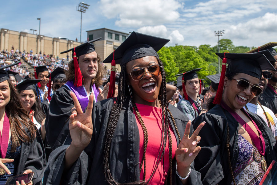 Graduating students in caps and gowns cheering during the Commencement ceremony at Gesling stadium.
