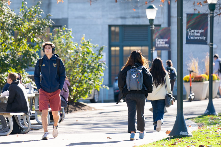 Student walking through campus with fallen leaves from nearby trees surrounding him on the walkway.