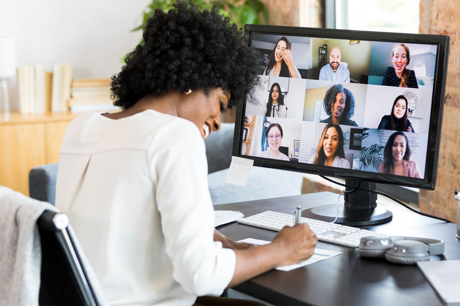 Woman participating in a web conferencing call and smiling as she writes on a piece of paper.