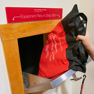 Image of the return drop slot with the drawer open and a hand dropping a bag of equipment in.