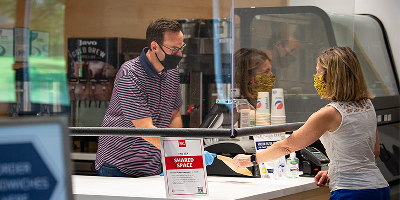 Photo of a person purchasing a soda from behind a protective barrier.