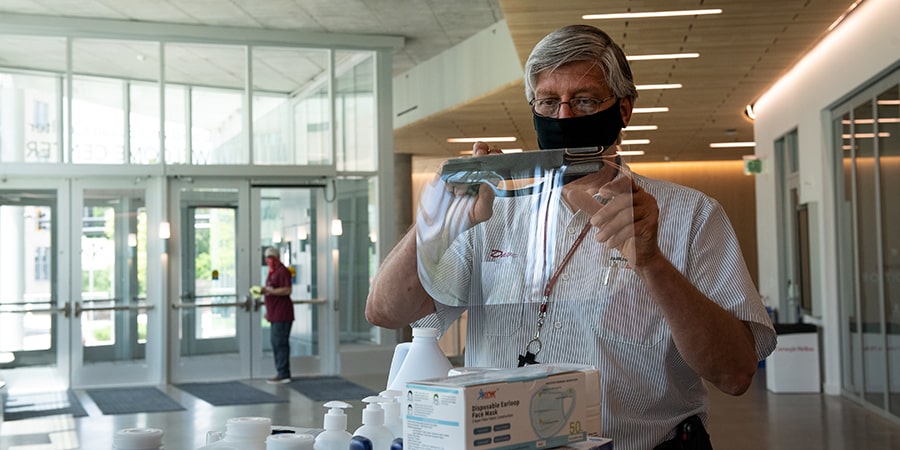 Man with grey hair holding up a large, clear, facial protection mask.