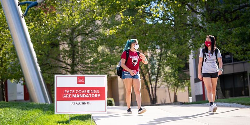 Photo of students walking with a face mask sign in front of them