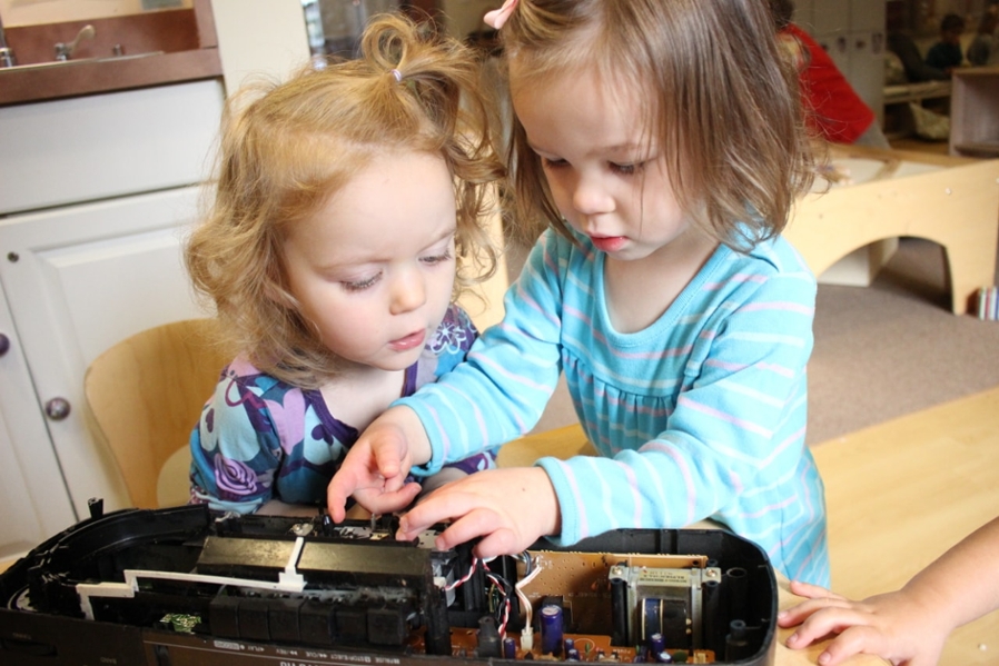 Two children tinkering with an old opened electronic device