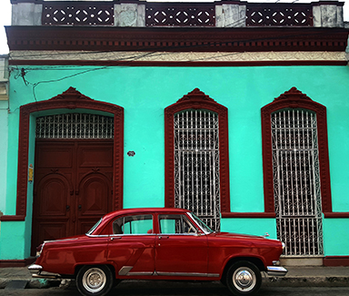 A photo of a retro car in front of a brightly colored building in Camaguey.