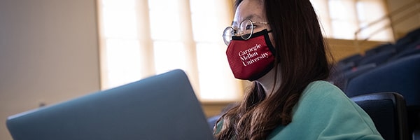 a student in class working on a laptop wearing a CMU face mask
