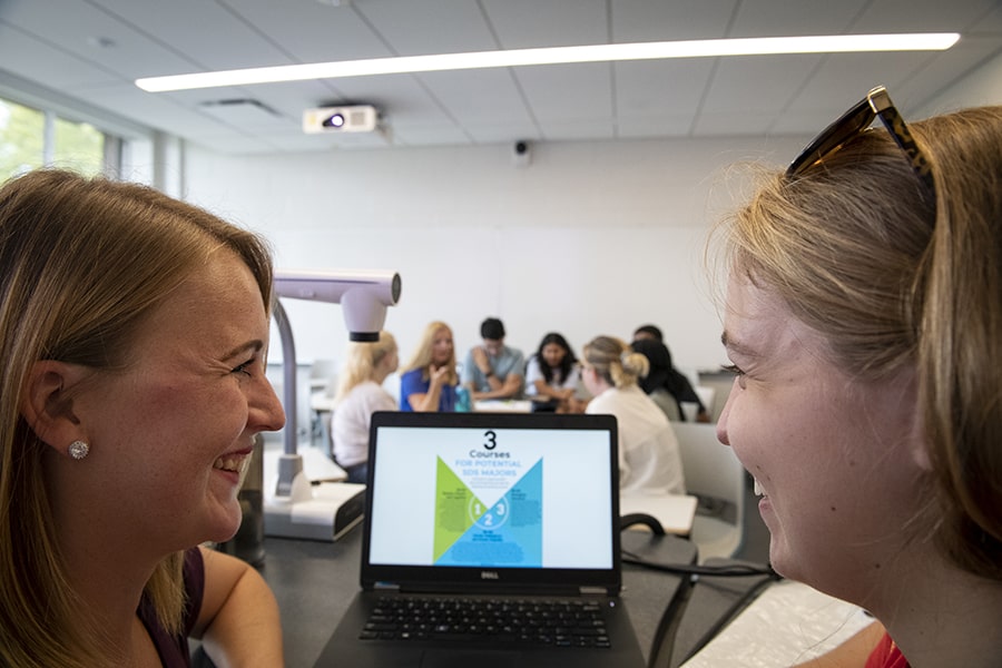 A student and advisor laugh while consulting a computer screen.