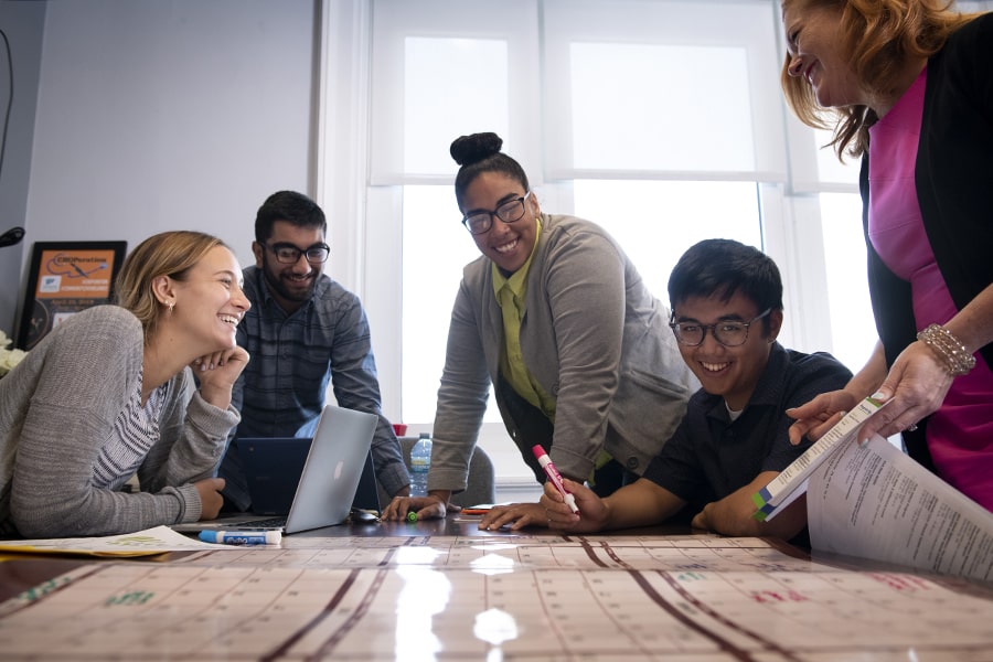 a smiling team works at a table, reviewing documents and writing on a planner