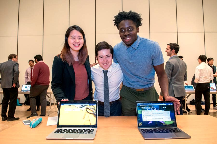Information Systems students pose behind a table with laptops open and facing the audience