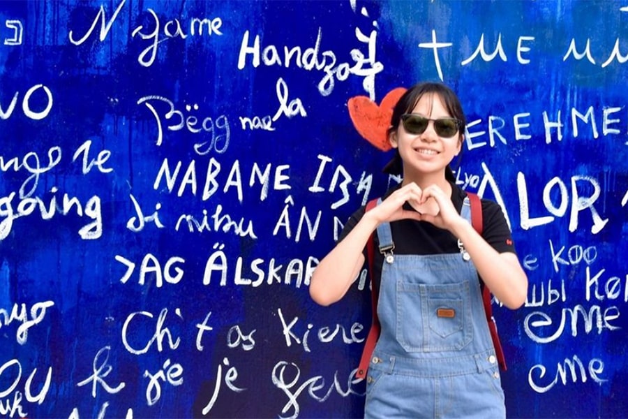 Kady Yip holding their hands in the shape of a heard in front of a blue mural