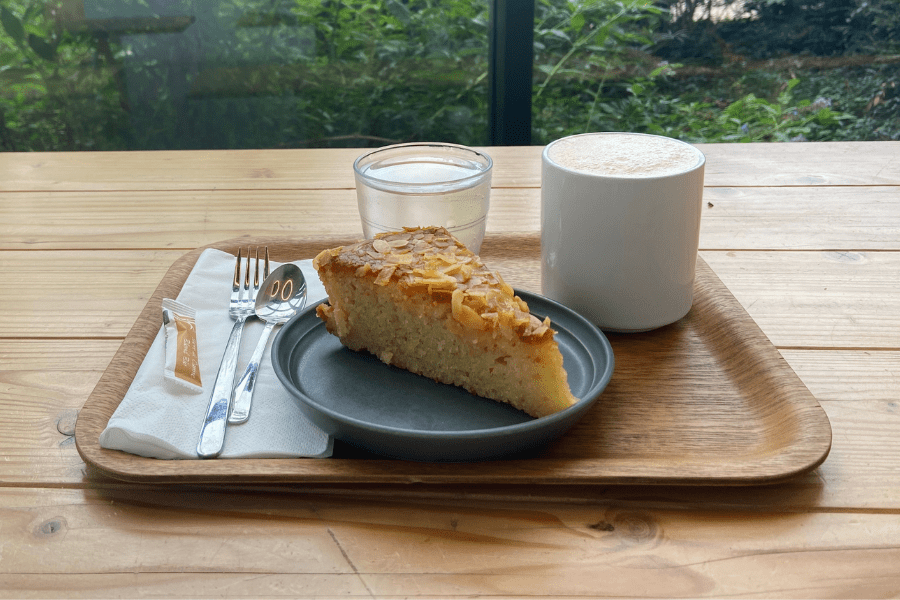 Wooden tray with a slice of cake, glass of water, and latte. 