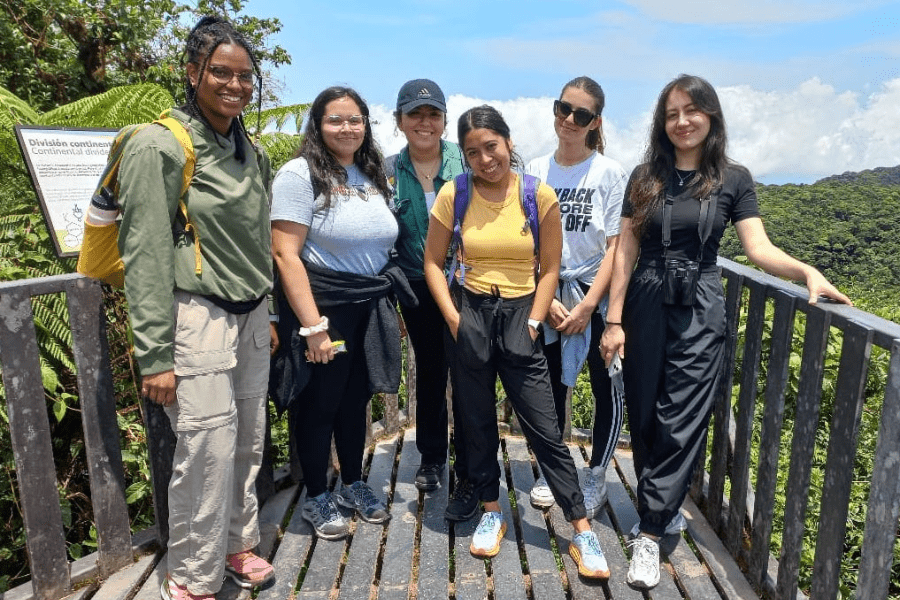 Six students pose outdoors for a photo in Monteverde, Costa Rica. The sky is blue and there is a lush forest behind them.