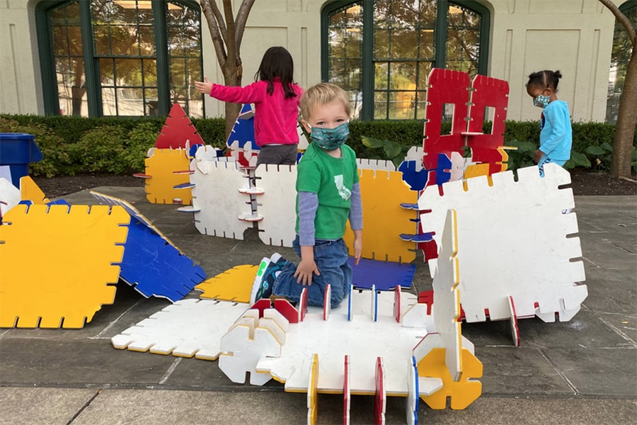 Children wearing masks, playing with architectural blocks outdoors