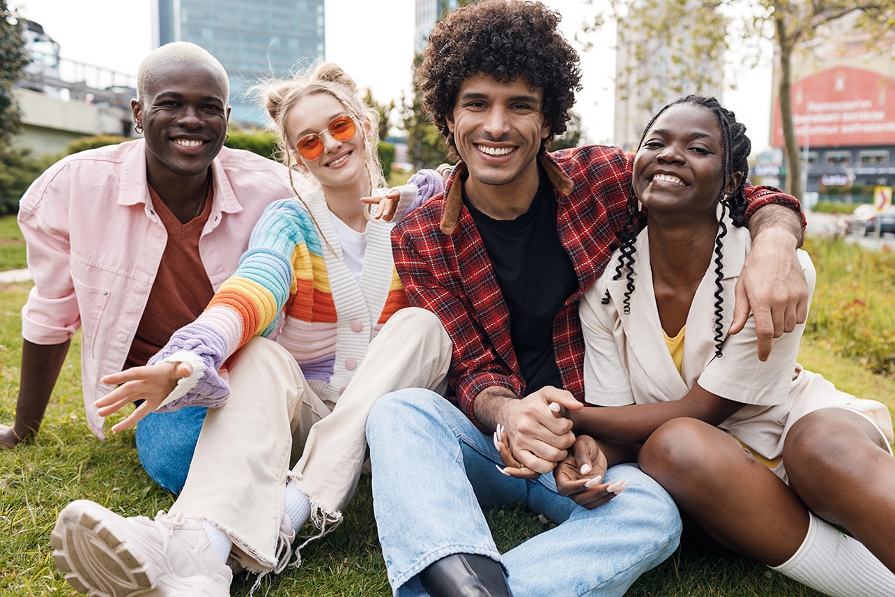 a group of friends sit in the grass with their arms and hands in contact with each other