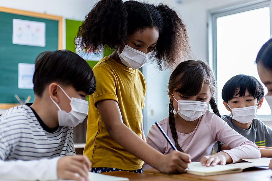 Masked grade school students work together at a table.