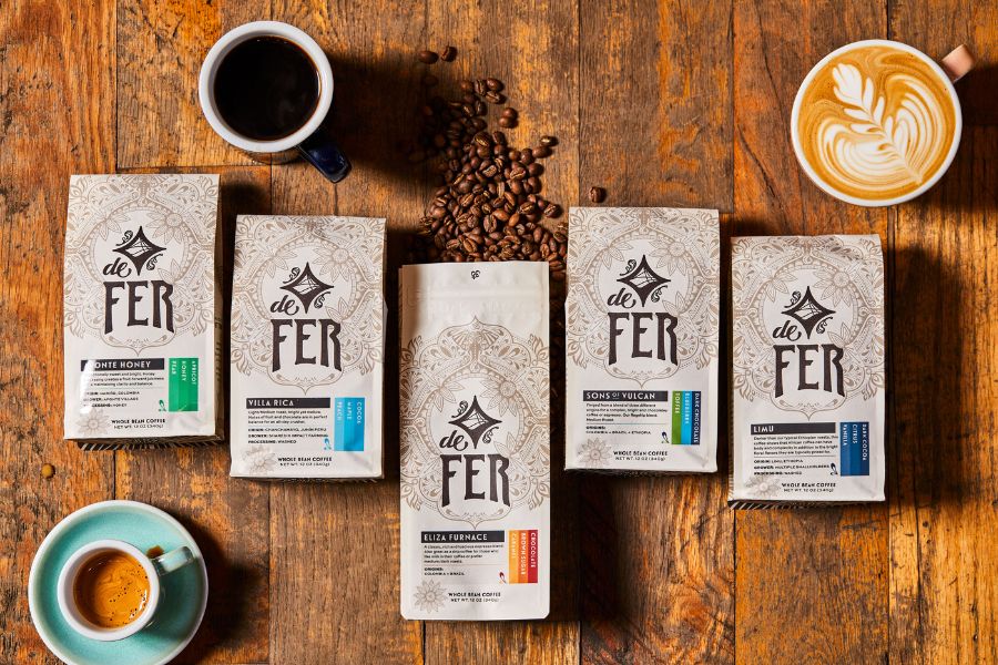 bags of De Fer coffee displayed on a wood background with coffee, espresso and a latte