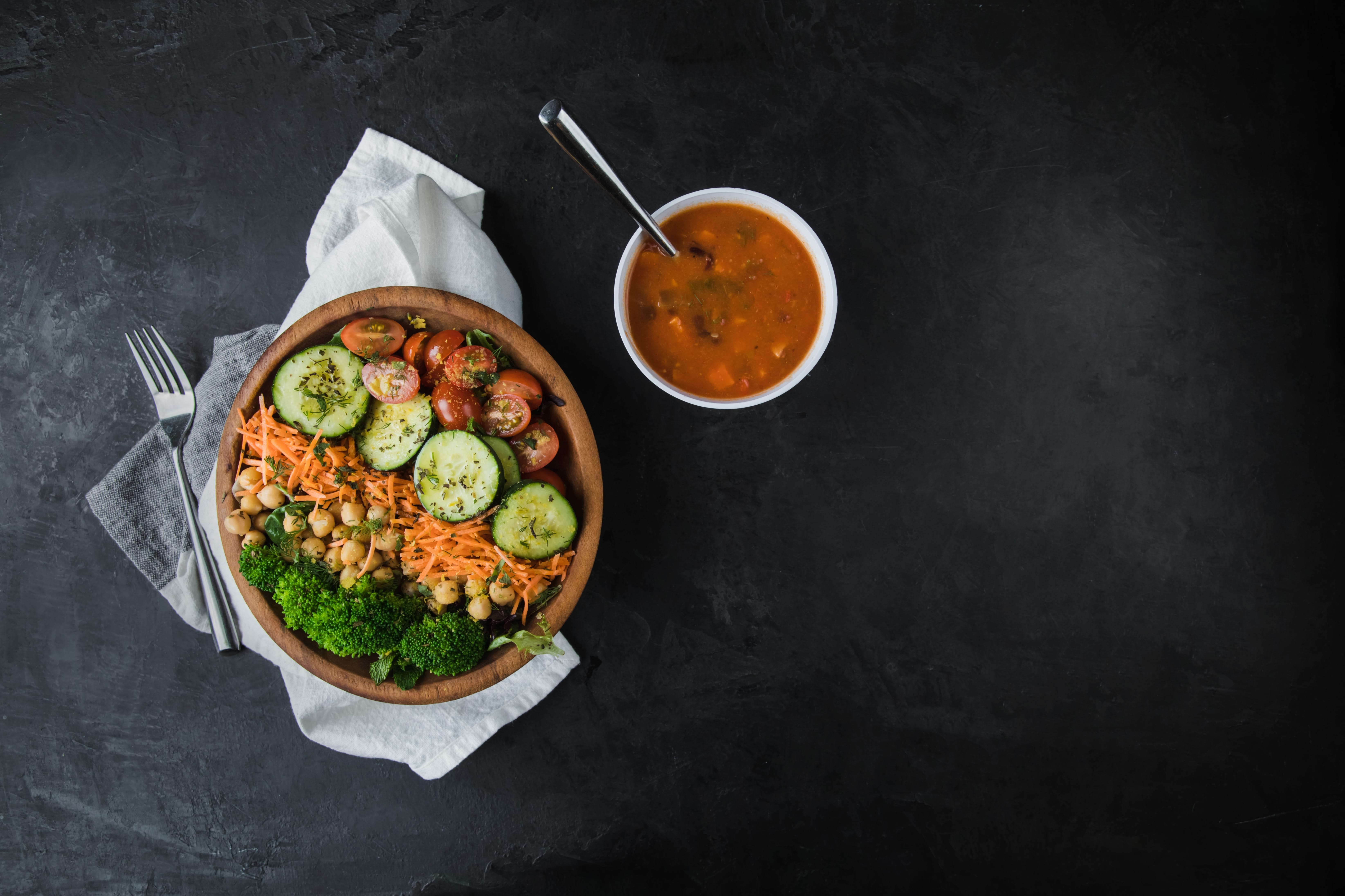 Photo of a salad with many different kinds of vegetables and a small bowl of tomato soup