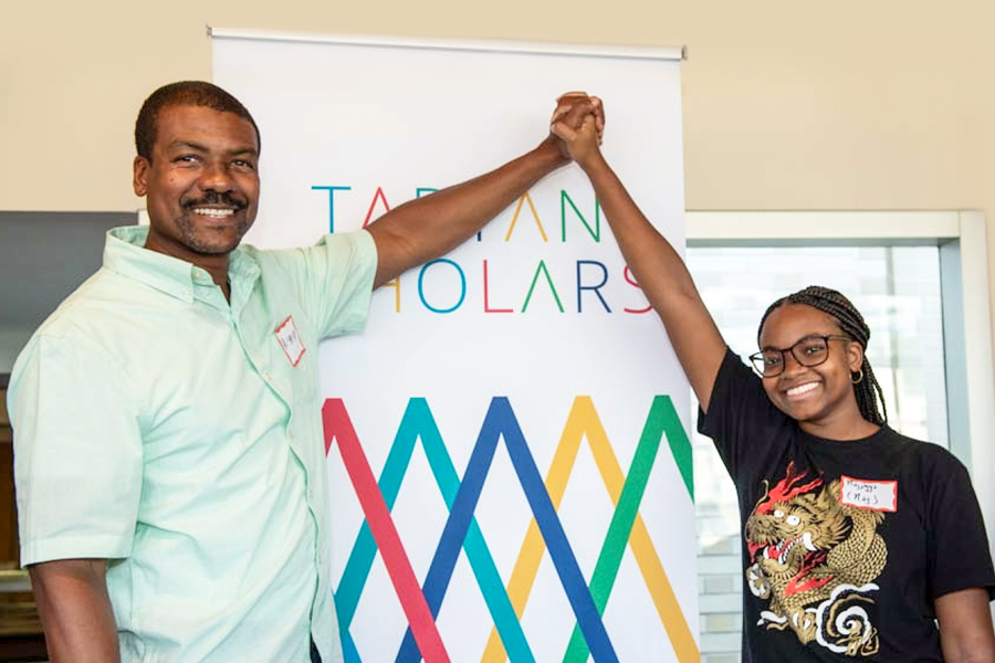 Man and woman hold hands in front of Tartan Scholars sign