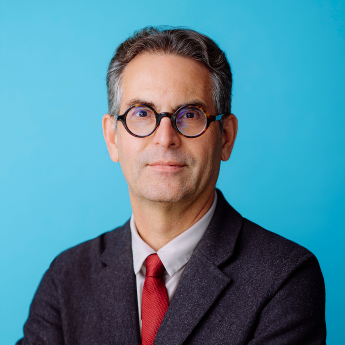Man with grey suit, red tie, white shirt, and black glasses