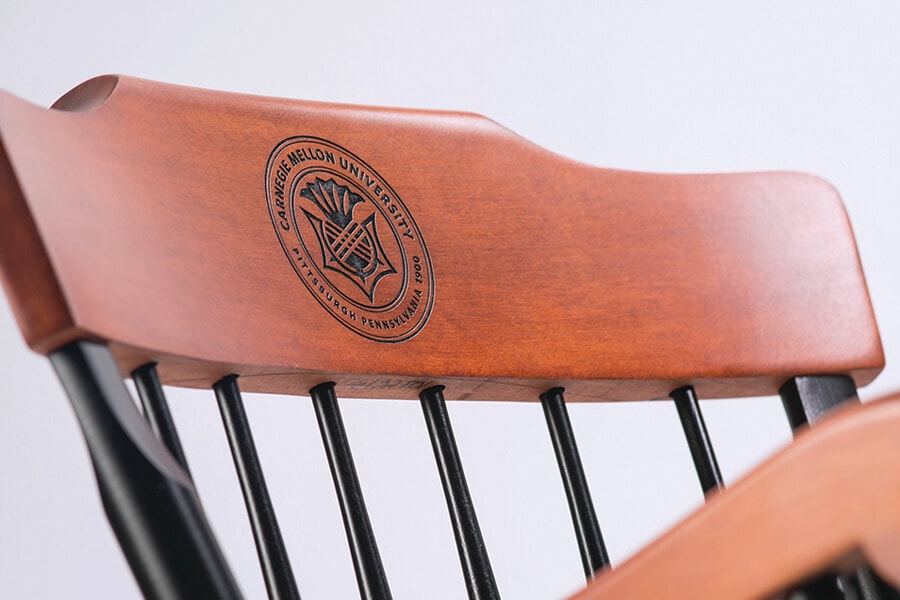 A close up picture of the top of a wooden chair, with the CMU logo in the top arch