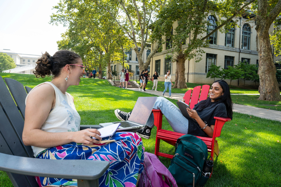 two female students sitting in chairs outside on a grassy area and talking 